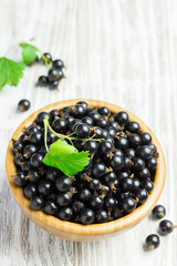 Ripe black currant in a wooden bowl on white shabby wooden table.  Selective focus, space for text.