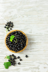 Ripe black currant in a wooden bowl on white shabby wooden table. Top view  space for text.