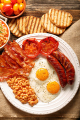 English Breakfast with sausages, grilled tomatoes, egg, bacon, beans and bread on white plate