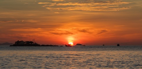 Obraz premium A fiery orange sunrise sky looking out over the south China sea in Nha Trang Bay Vietnam. With fishing boats in silhouette.