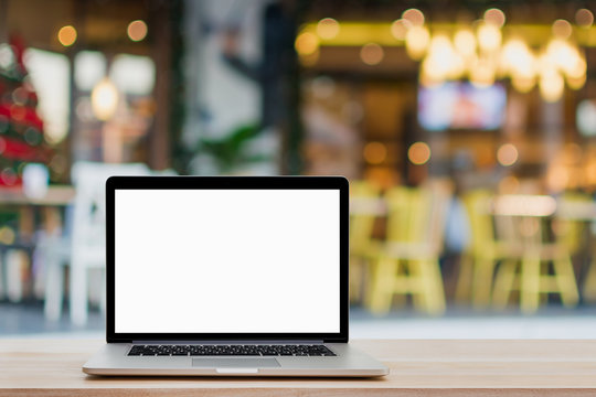 Laptop with blank screen on wood table and coffee shop background.