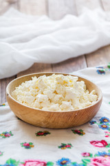 Cottage cheese in a wooden bowl on a background of cans of milk