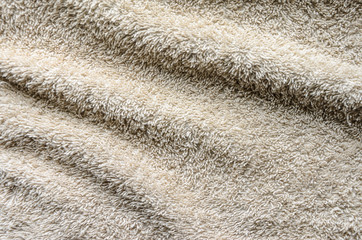 Casually lying towel of beige color. Folds on the surface of a beige towelbackground