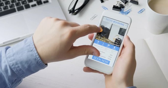 Man booking room in the apartment using his smartphone and online booking mobile app sitting at his desk