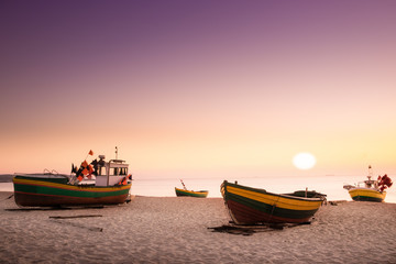  Sun just rises over colorful fishing cutters on sandy beach. Baltic sea.