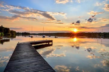 Fototapeta premium Summer afternoon landscape. Wooden pier and boat on the water at sunset.