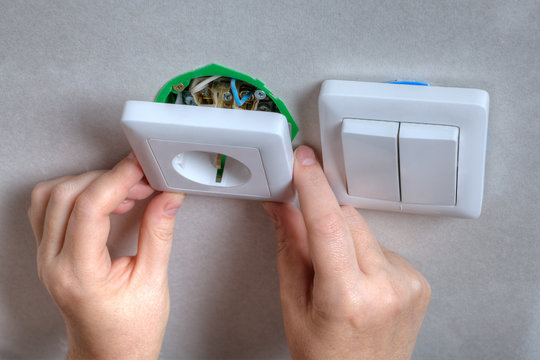 Installing the wall outlet into a wiring box, close-up hands.