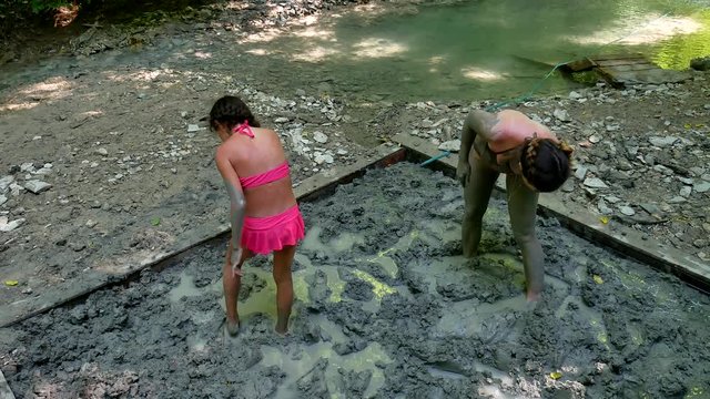 Woman and girl teen tourist in bathing suit is smeared with curative clay on the nature of mountain forest. girl medicine skin treatment