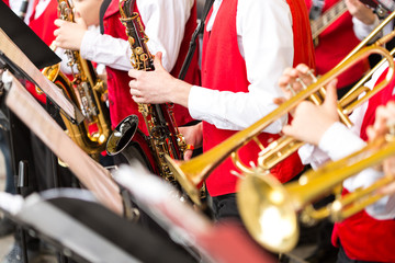 jazz band music performance concept - orchestra of wind instruments during the concert, selective focus on hands of musicians playing on trumpets and saxophones, closeup male in red costumes