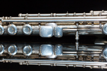 symphonic music concept - closeup on western concert flute lies on the pure black mirror surface, middle body section of instrument with majority of keys, marching, orchestra concerts, macro © melnikofd