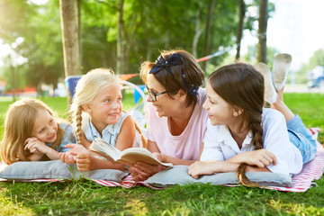 Restful girls and their mother reading book and discussing it in park