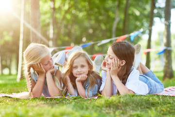Naklejka premium Three cute girls relaxing on green lawn in summer park