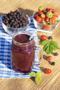 Strawberry, raspberry, blackberry and banana juice smoothie shake in glass mug, outdoors, close up