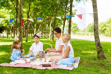 Three girls and their mother enjoying picnic on green lawn in summer park