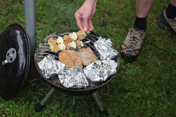man putting skewers on barbecue with steaks and vegetables in foil