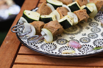 vegan skewers with seitan onions and zucchini on pretty plate on wood table