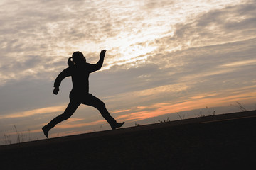 Silhouette of man exercising running up the hill against the sunset