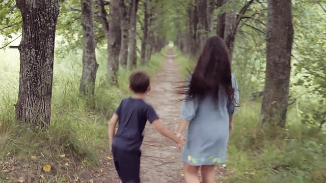 Cute happy little girl and boy running through the forest holding hands smiling. Brother with sisters for a walk