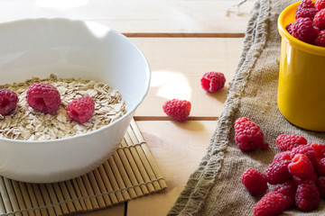 Bowl of oatmeal porridge with fresh raspberries, muesli on wooden table. Healthy breakfast concept