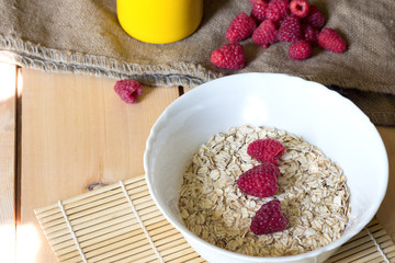 Bowl of oatmeal porridge with fresh raspberries, muesli on wooden table. Healthy breakfast concept