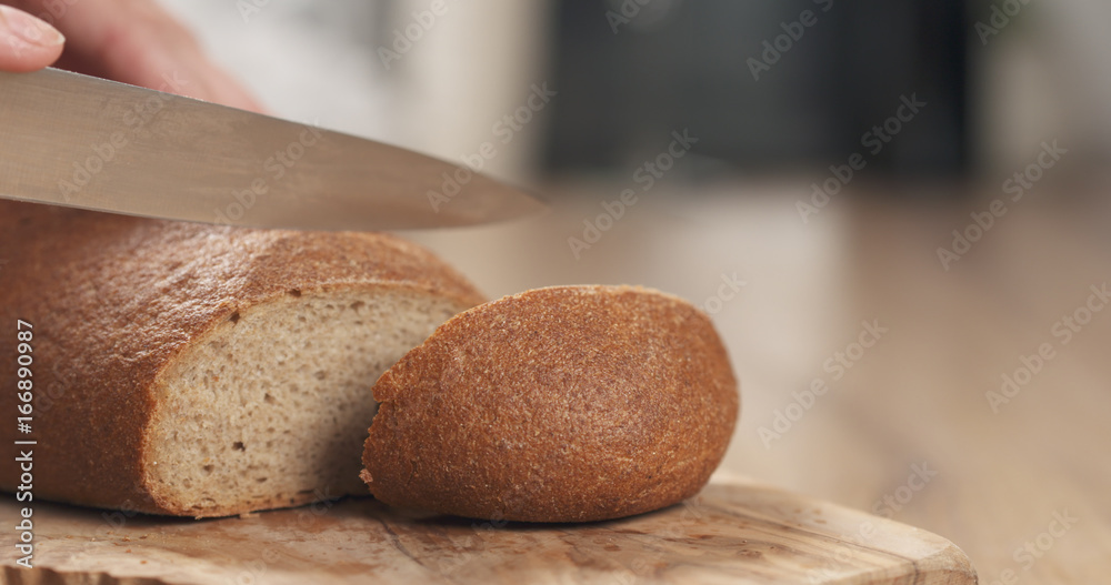 Wall mural young female hands slicing rye wheat rustic bread on cutting board