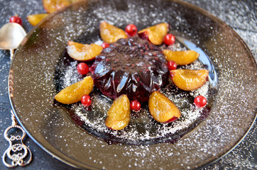 cool burgundy jelly with berries and powder decorated with fresh plums, red currant and silver vintage spoon on a dark brown plate on black wooden background close up. Side view
