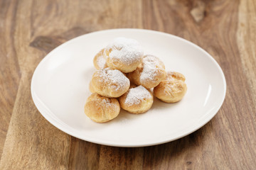 profiteroles covered with sugar powder on white plate on wooden table