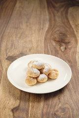 profiteroles covered with sugar powder on white plate on wooden table