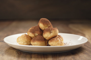 profiteroles covered with cocoa powder on white plate on wooden table