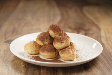 profiteroles covered with cocoa powder on white plate on wooden table