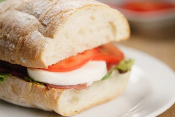 closeup shot of ciabatta sandwich with speck, mozzarella and vegetables