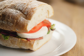 closeup shot of ciabatta sandwich with speck, mozzarella and vegetables