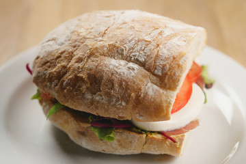 closeup shot of ciabatta sandwich with speck, mozzarella and vegetables