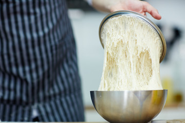 Baker checking sourdough starter in metallic bowl