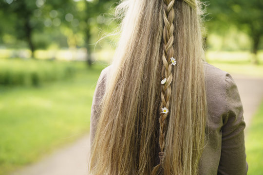 teen girl with daisy flowers in hair in green park from behind in summer day