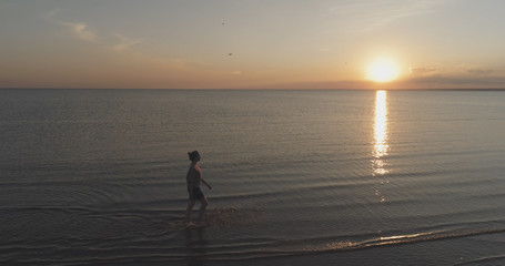 Aerial shot over teen girl barefoot walking in water on baltic sea beach in sunset time