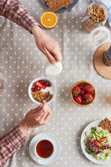 Man adding milk into bowl with muesli while having breakfast