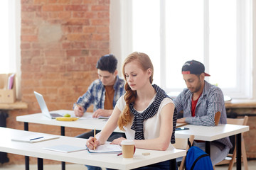 Young managers writing examination essay by desks