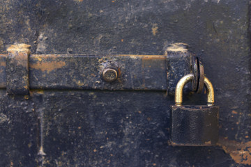 Close up detailed view of an old black door with an iron padlock.