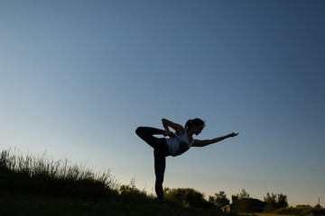 Woman doing yoga outdoor. Young woman exercising meditation for fitness lifestyle at the nature background with blue sky. Concept Yoga freedom silhouette on sunset, full length shot with copy space