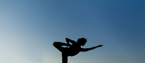 Fototapeta premium Woman doing yoga outdoor. Young woman exercising meditation for fitness lifestyle at the nature background with blue sky. Concept Yoga freedom silhouette on sunset, full length shot with copy space