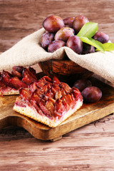 rustic plum cake on wooden background with plums around
