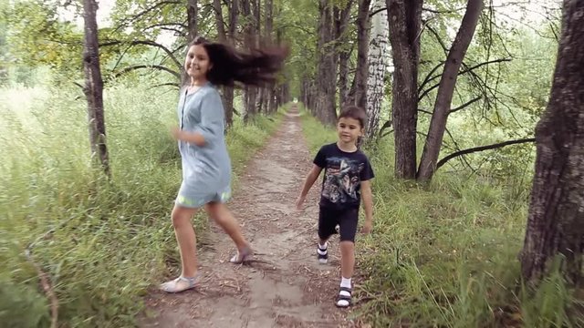 Cute happy little girl and boy are running through the forest in summer in sunny weather