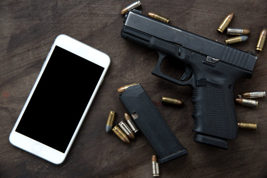 Gun with ammunition and mobole phone on dark background. 