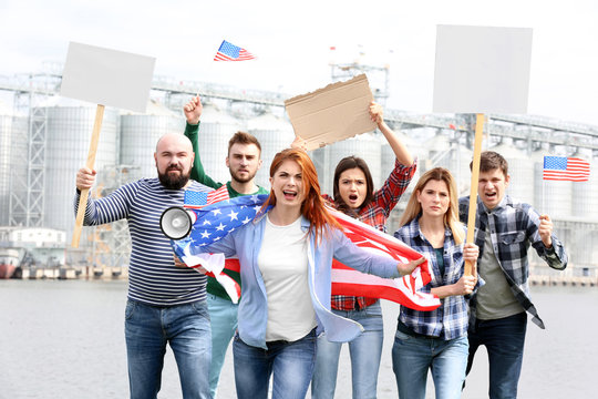 Group of protesting young people with American flag and factory on background