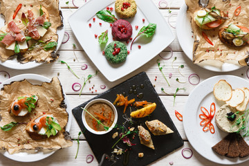 Dinner table with different appetizers. Snacks, paste and small canapes with spices decoration on wooden white background