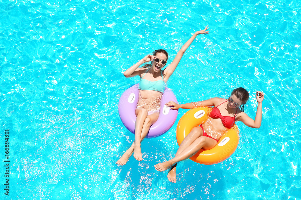 Wall mural Beautiful young girls with inflatable rings in blue swimming pool