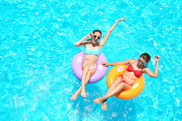 Beautiful young girls with inflatable rings in blue swimming pool