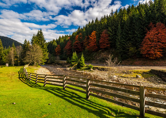 fence on the meadow near forest river in autumn mountains