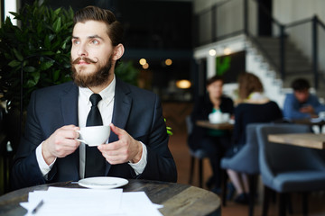Pensive agent with cup of coffee having minute of rest in cafe